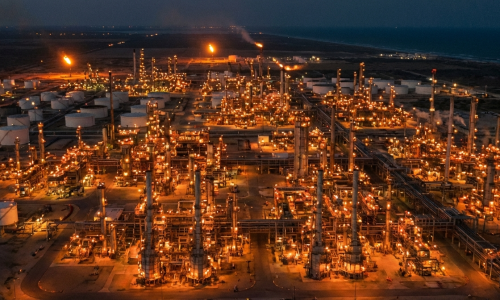 Vista aérea cinematográfica de una refinería de petróleo masiva en Texas de noche con luces industriales naranjas